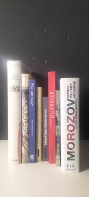 Plusieurs livres sont alignés sur une étagère devant un mur noir