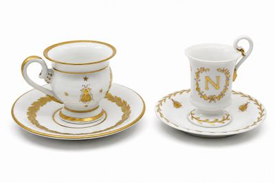 deux tasses à café blanches et dorées avec leurs soucoupes, posées sur une surface blanche