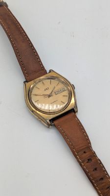 une image d'une montre sur une surface blanche avec un bracelet marron