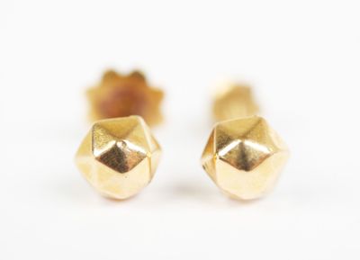 two gold stud earrings on a white surface with a white background