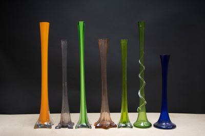 Plusieurs vases en verre de différentes couleurs sont alignés sur une table