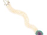 a close up of a bracelet with pearls and a purple stone