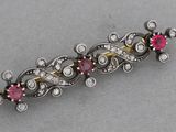 a close up of a silver and gold broochle with pink stones