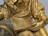 a gold statue of a man reading a book and holding a clock