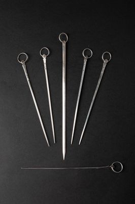 four pairs of scissors and a needle on a black surface