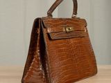 brown alligator skin handbag on a wooden table with a curtain in the background