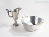 un bol en argent et une coupe en argent posés sur une table blanche