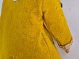 doll sitting on a stool wearing a yellow coat with a tag on it