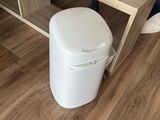 a white trash can sitting on the floor next to a wooden shelf