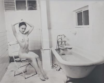 photographie en noir et blanc d'une femme nue assise sur une chaise devant une baignoire
