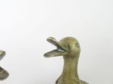 two bronze ducks standing next to each other on a white surface