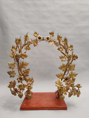 une image représentant une couronne dorée ornée de feuilles et de fleurs, posée sur un socle rouge