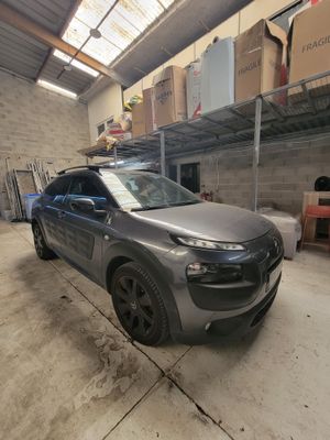 La voiture grise est garée dans le garage, devant des cartons.