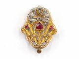 une image représentant une broche en or ornée de pierres rouges et de feuilles