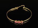 a gold bracelet with pink stones on a black background