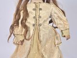 a close up of a doll with long hair wearing a gold dress