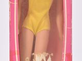 une poupée Barbie dans une boîte rose, vêtue d'un haut jaune et de chaussures bleues