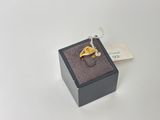 une photo d'une bague en or dans un coffret noir, accompagnée d'une étiquette