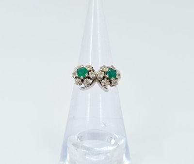 une photo d'une paire de boucles d'oreilles en émeraude et diamant posées sur un socle en verre transparent