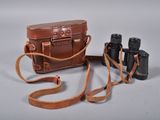 a brown bag with a brown strap and a pair of binoculars next to it