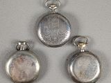three silver pocket watches sitting next to each other on a white surface