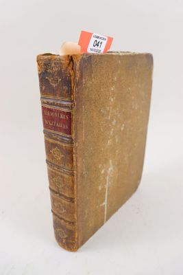 un vieux livre posé sur une surface blanche, sur lequel est accrochée une étiquette