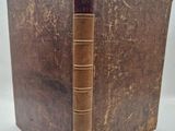 an old book with a brown cover sitting on top of a white table