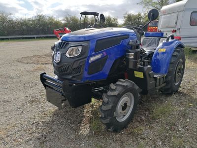 un tracteur bleu garé sur la terre battue