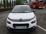 une voiture blanche garée sur un parking, avec un camion de pompiers en arrière-plan