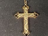 a gold cross pendant with filigree design on a black background