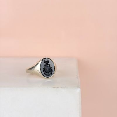 a close up of a silver signet ring with a black wax seal on it