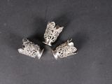 three silver napkin rings with crowns on them on a black surface