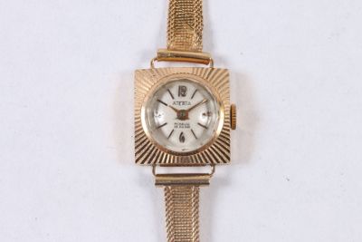 une montre-bracelet en or avec un cadran blanc sur une surface blanche