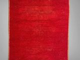 a red rug with fringes hanging on a gray wall