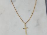 un pendentif en forme de croix en or, suspendu à une chaîne en or, posé sur une surface en marbre