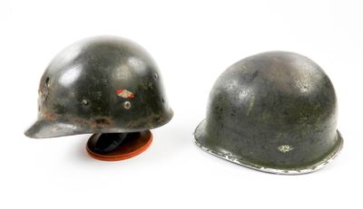 paire de casques allemands en acier de la Seconde Guerre mondiale, posés sur un socle, sur fond blanc