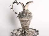 un plateau ancien en argent sur lequel est posé un vase en argent, le tout sur un fond blanc