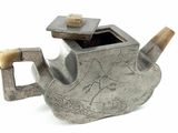 a silver teapot with a bird design on it