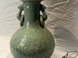 a green vase with a lamp on a white table