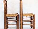 pair of wooden chairs with rattan seats against a white wall