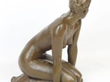 statue of a naked woman sitting on her knees on a white surface