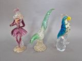 trois figurines en verre représentant une femme et un oiseau, posées sur un socle