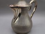 an antique silver coffee pot with a lid on a gray surface