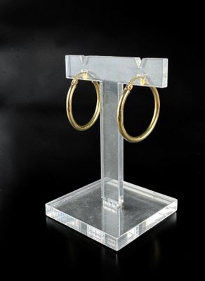 a close up of a pair of gold hoop earrings on a clear stand