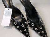 les chaussures sont noires, ornées de cercles argentés, et portent une étiquette de prix