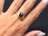 the woman is wearing a gold ring with a black stone on it
