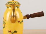 a yellow tea pot with a wooden handle on a table