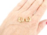 a woman ' s hand holding a pair of gold earrings