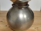 a silver vase on a wooden table with a shelf in the background