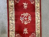 tapis accroché au mur d'une pièce où se trouve un tapis rouge et blanc